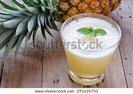 Glass of pineapple smoothie with fresh mint leaves and pineapple on wooden table