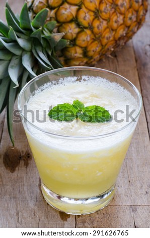 Glass of pineapple smoothie with fresh mint leaves and pineapple on wooden table