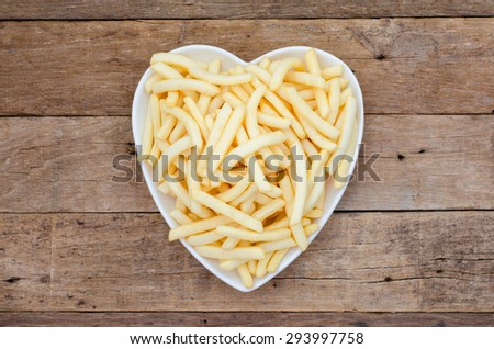 Potato french fries flavor snack in heart-shaped plate prepared on wooden table (top view from above)