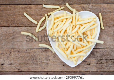 Potato french fries flavor snack in heart-shaped plate prepared on wooden table (top view from above