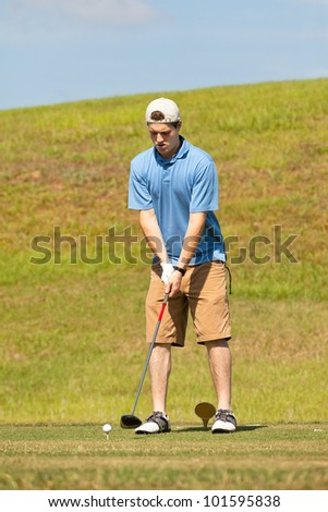 Young male golfer setting up to hit from the tee box.