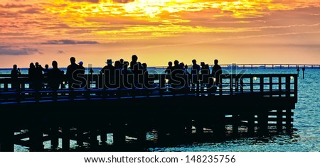 Pier filled with people enjoying a golden glow sunset in Destin, Florida