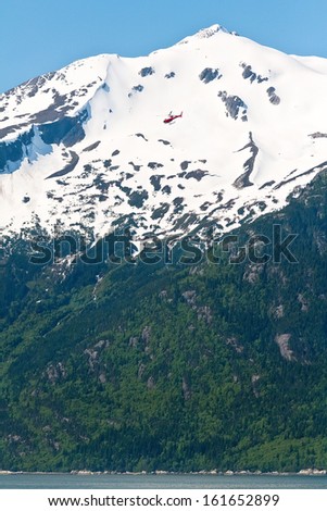 Helicopter flying high against the snow capped mountain peak in Skagway, Alaska