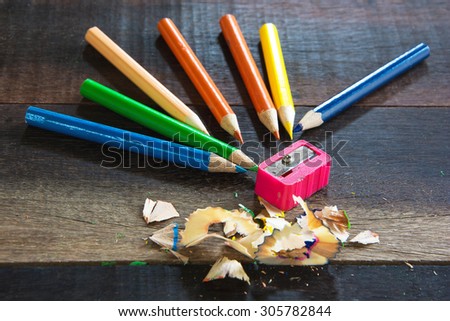 COLOR PENCILS AND PENCIL SHARPENER ON THE VINTAGE WOODEN TABLE TEXTURE BACKGROUND\
(SELECTIVE POINT FOCUS)