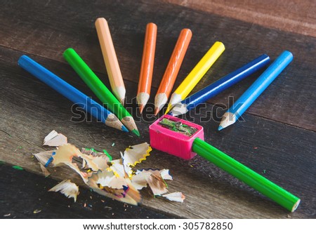 COLOR PENCILS AND PENCIL SHARPENER ON THE VINTAGE WOODEN TABLE TEXTURE BACKGROUND\
(SELECTIVE POINT FOCUS)