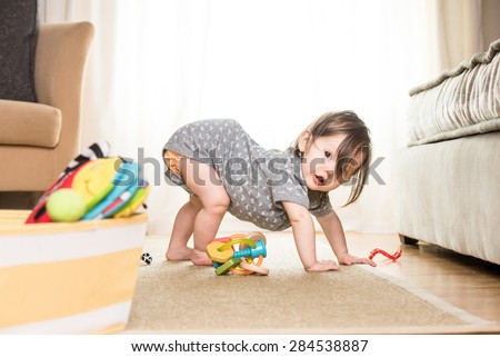 Baby playing and crawling around, making faces, on a rug on the floor.