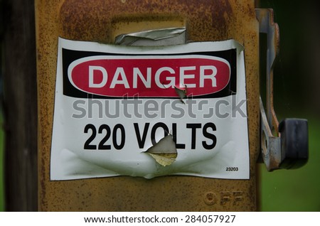 Electrical danger sign that is weathered, worn and neglected.  The sign is on an electrical box that is in much worse condition.
