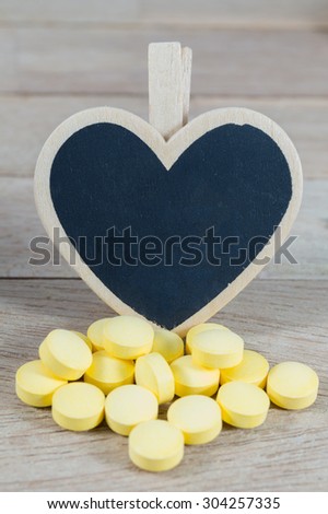 Yellow pills  with blank heart shape blackboard on wood background