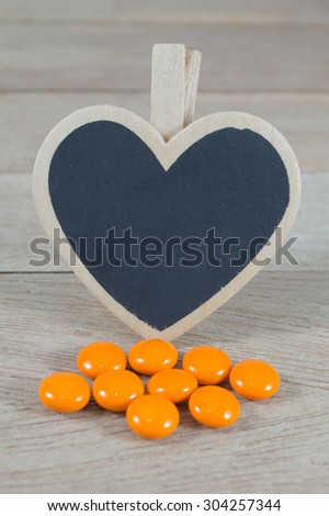 Orange pills  with blank heart shape blackboard on wood background