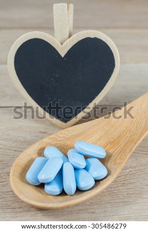 Blue pills in wooden spoon with blank heart shape blackboard