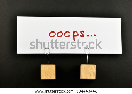 Oops, one big white paper note with two wooden holders isolated on black paper background for presentation