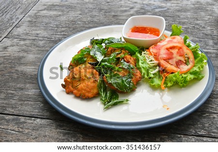 Plate of fish and shrimp deep fried cakes croquettes snack with salad basil leaves and hot sauce on vintage wooden table surface