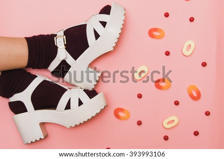 Flat lay fashion set: woman\'s legs in dark red socks, white shoes and candies on pink pastel palette background