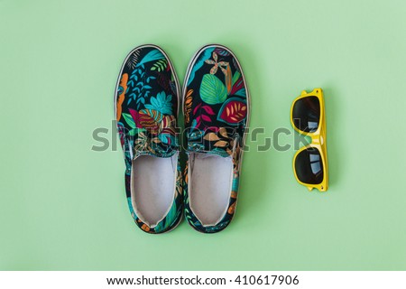Flat lay fashion set: colored slippers shoes with palm and flowers print and yellow sunglasses on pastel background. Top view.