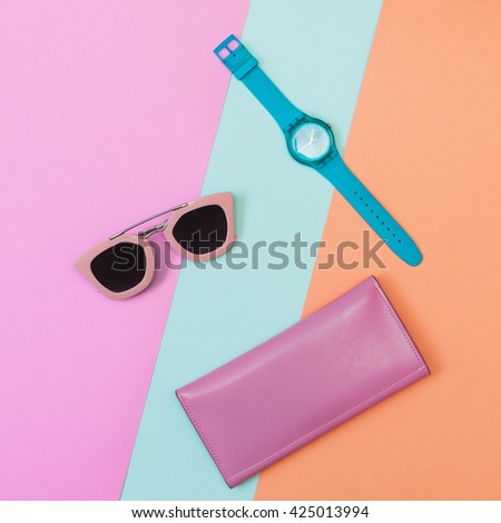 Flat lay fashion set:  mint blue watch, sunglasses and pink purse on pastel blue, pink and rose quartz colored backgrounds. Top view.