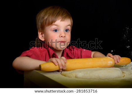 The child knead the flour, the dough with a rolling pin rolls. On a black background
