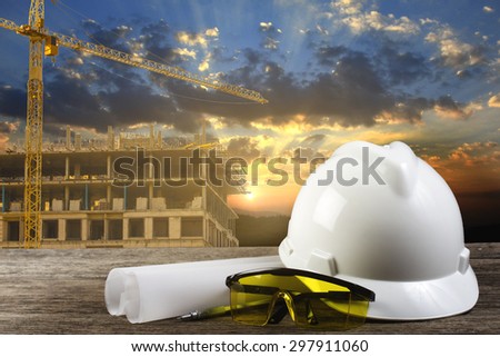 file of safety helmet and architect plant on wood table with sunset scene and building construction