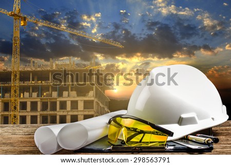 file of safety helmet and architect plant on wood table with sunset scene and building construction
