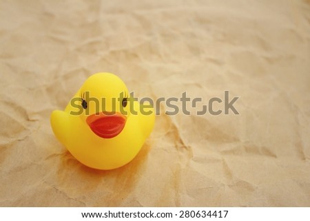 Yellow rubber duck on background of light brown.