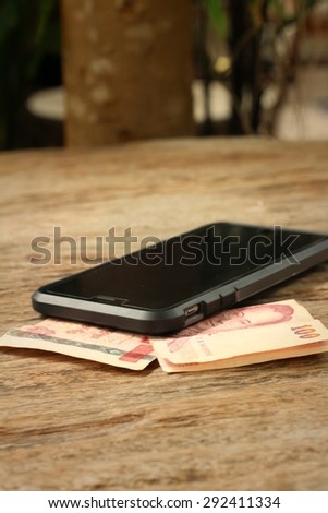 Smart phone with money of Thai Bath on wooden background.