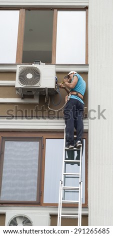 man standing on a ladder and sets the air conditioner outdoor unit