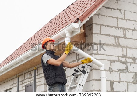 construction worker installs the gutter system on the roof