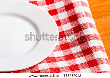 empty white plate on a red and white tablecloth