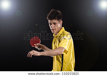 young man tennis-player in play on black background with lights