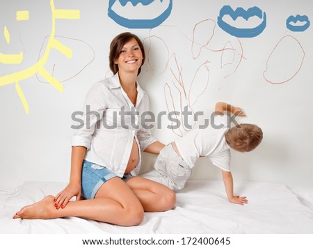 pregnant mother with her son on white bed. Child draws on the wall