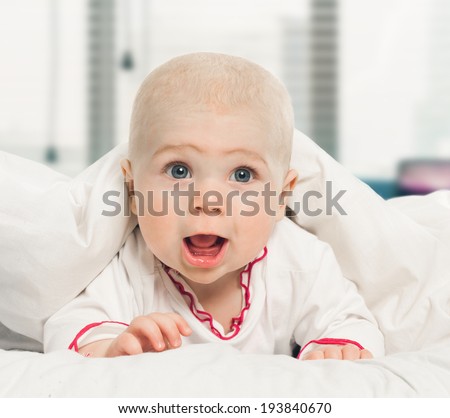Adorable baby, looking out under a white blanket, cover. on window background