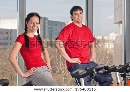 People exercising on bicycles in fitness gym. Couple exercising by spinning on stationary bicycles.