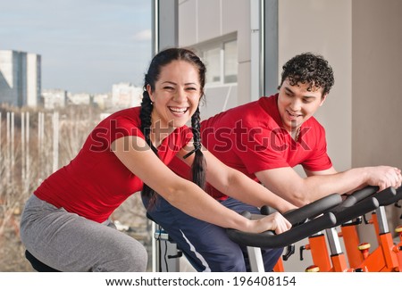 People exercising on bicycles in fitness gym. Couple exercising by spinning on stationary bicycles.