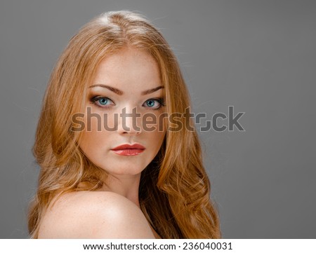 beautiful young redhead woman with freckles portrait isolated on grey background