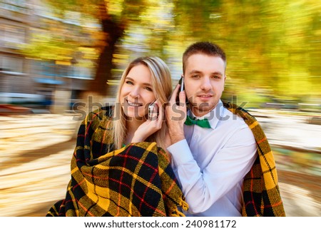 couple having fun on spinning roundabout and using a mobile phone. Autumn. Naturally blur motion