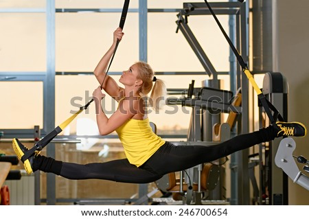 Young attractive woman does splits crossfit stretching with trx fitness straps in the gym\'s studio