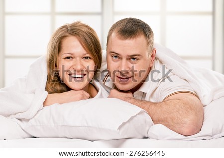 Happy smiling couple laying laughing in bed on light window background