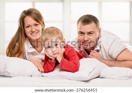 A young family with little daughter to bed in the bedroom on window background