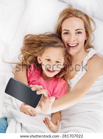 happy mother with daughter on white bed and make a selfie, shot from above