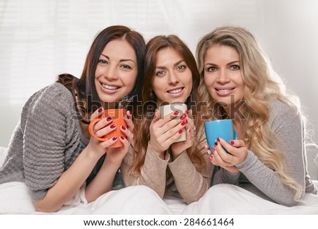 three female friends portrait with cups on the bed on light window background