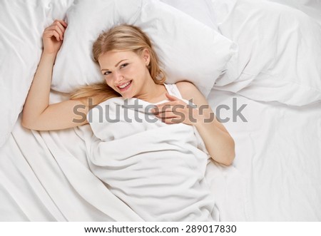 Young beautiful happy woman waking up on bed, shot from above