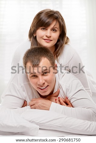 Happy smiling couple laying laughing in bed with light window background