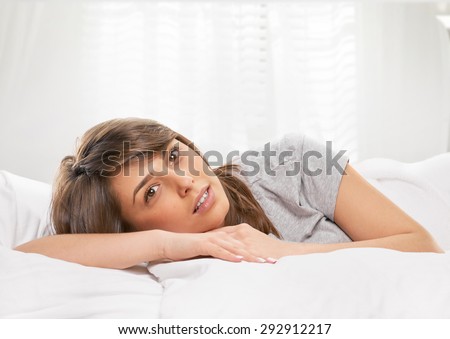 young woman sitting in bedroom at early morning, on light window background