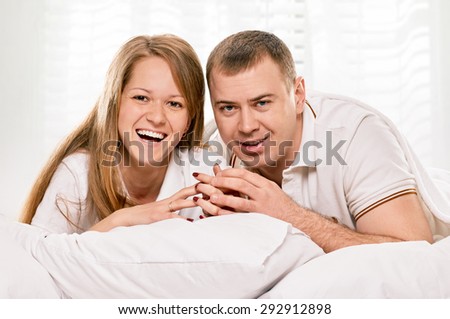 Happy smiling couple laying laughing in bed on light window background