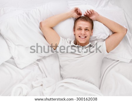 Young handsome happy man waking up on bed, top view
