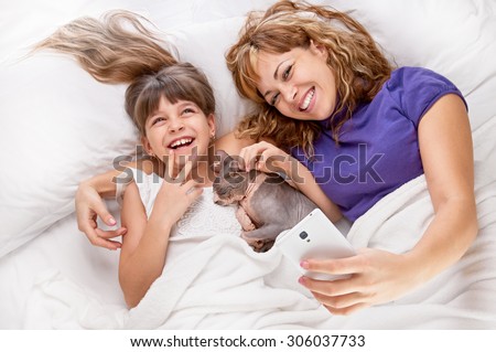 happy mother with little daughter and cat sphynx on white bed, shot from above