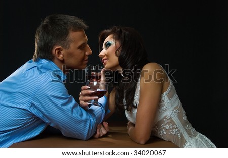 young loving couple sits at the table on black background with glass