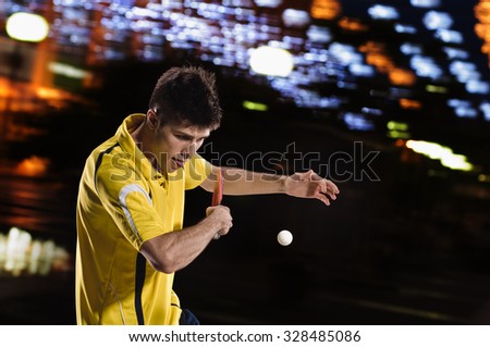 young sports man tennis-player in play on black background with  night lights