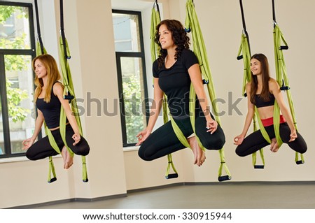Young women making antigravity yoga exercises. green hammocks