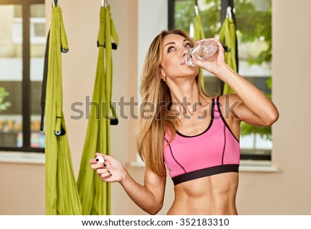 Young woman posing and drinking about anti-gravity aerial yoga green hammock indoor, with bottle water
