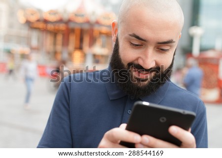 Outdoor portrait of modern bearded bald man with tablet in the street